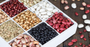 Box of assorted dried beans and lentils with scattered legumes on a wooden surface.